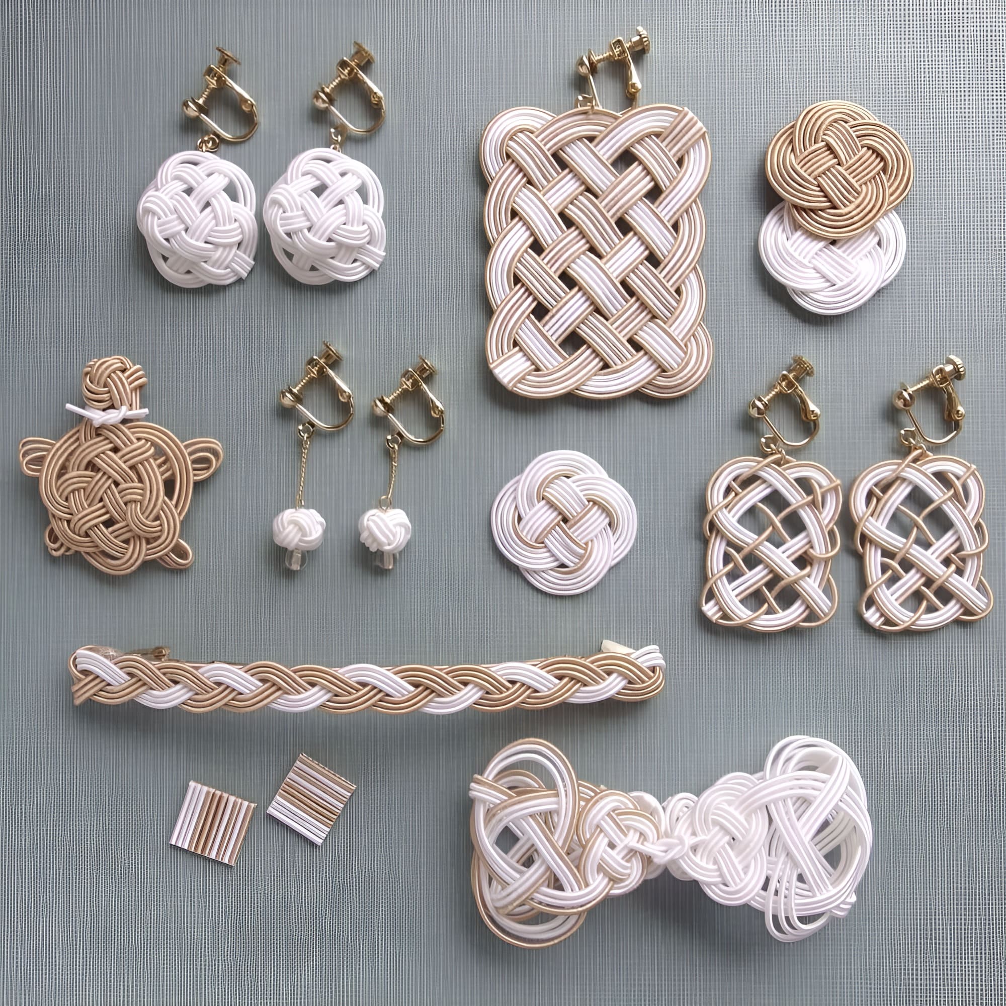 Mizuhiki earrings and accessories in white and soft brown arranged on gray fabric.